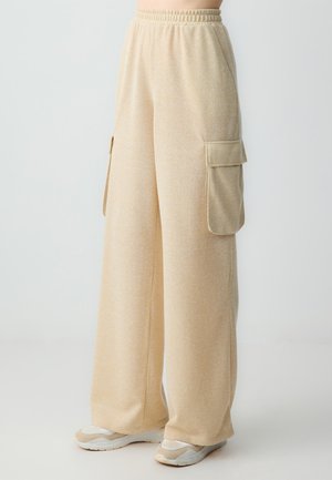 Pantalons cargo beige clair à jambes larges en tissu doux, dotés de deux poches latérales et d'une taille élastique pour le confort. Fini texturé.