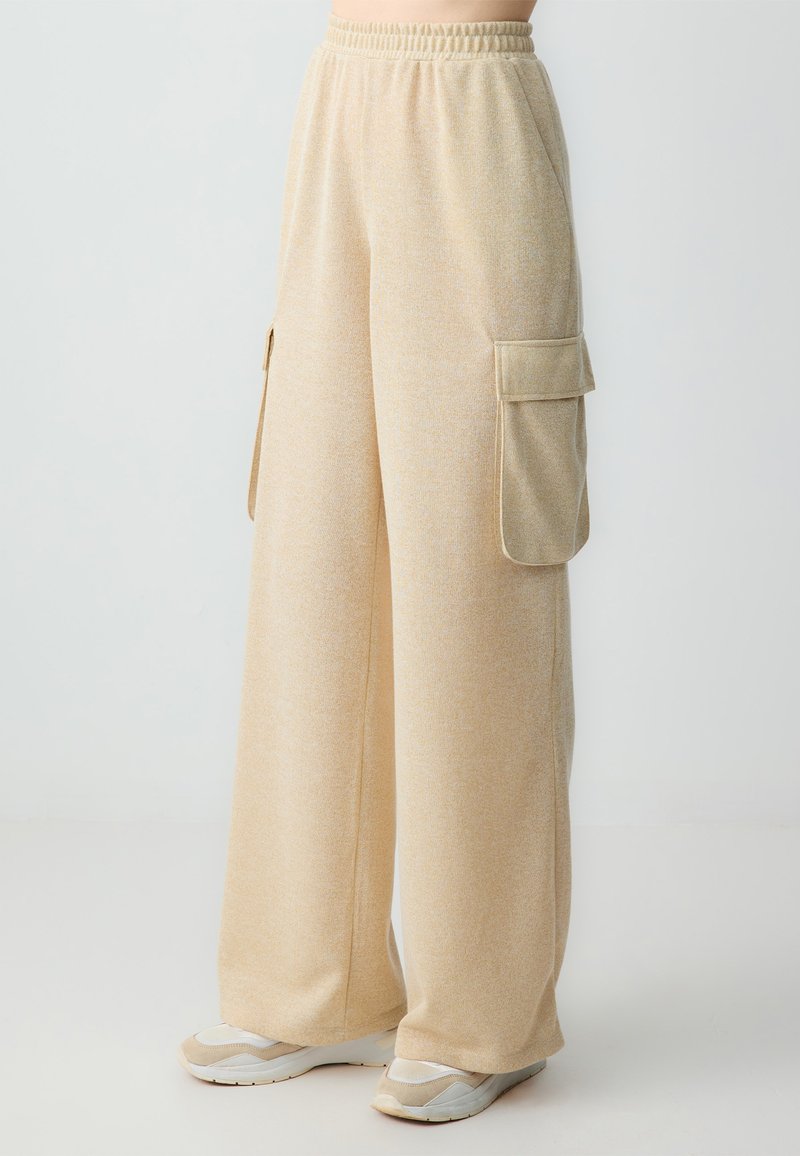Pantalons cargo beige clair à jambes larges en tissu doux, dotés de deux poches latérales et d'une taille élastique pour le confort. Fini texturé.