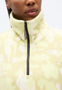 Φωτεινό κίτρινο φλις πουλόβερ με φερμουάρ στο μισό μήκος, με απαλή υφή και αφηρημένα λευκά σχέδια. Το λογότυπο της The North Face είναι κεντημένο σε λευκό.