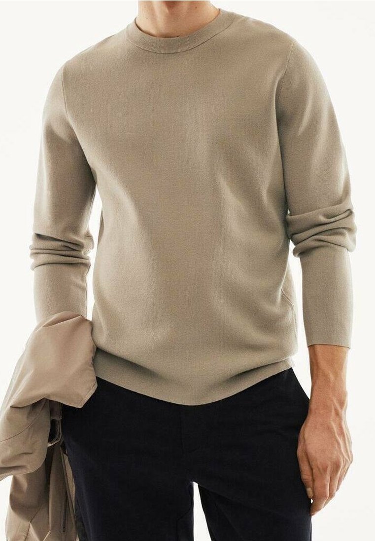 Beige svetr z bavlněné směsi s dlouhými rukávy, kulatým výstřihem, vroubkovanou texturou a mírně zakřiveným spodním lemem, doplněný béžovou bundou.