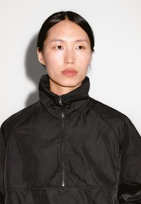 Giacca nera a mezza zip con colletto alto, caratterizzata da una texture liscia e un design minimalista, adatta per l'abbigliamento casual o sportivo.