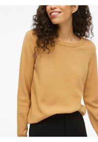 Sinise kollane kudumiga sviiter ümmarguse kaelusega, ribadega varrukaotsad ja mugav lõige, koos mustade pükstega. Pehme tekstuur.