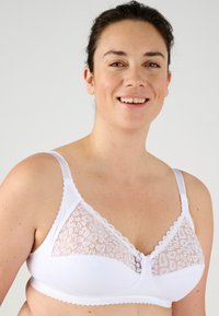 Sostén blanco con encaje en forma triangular. Presenta bordes festoneados, tirantes ajustables y un pequeño detalle de lazo en el centro.