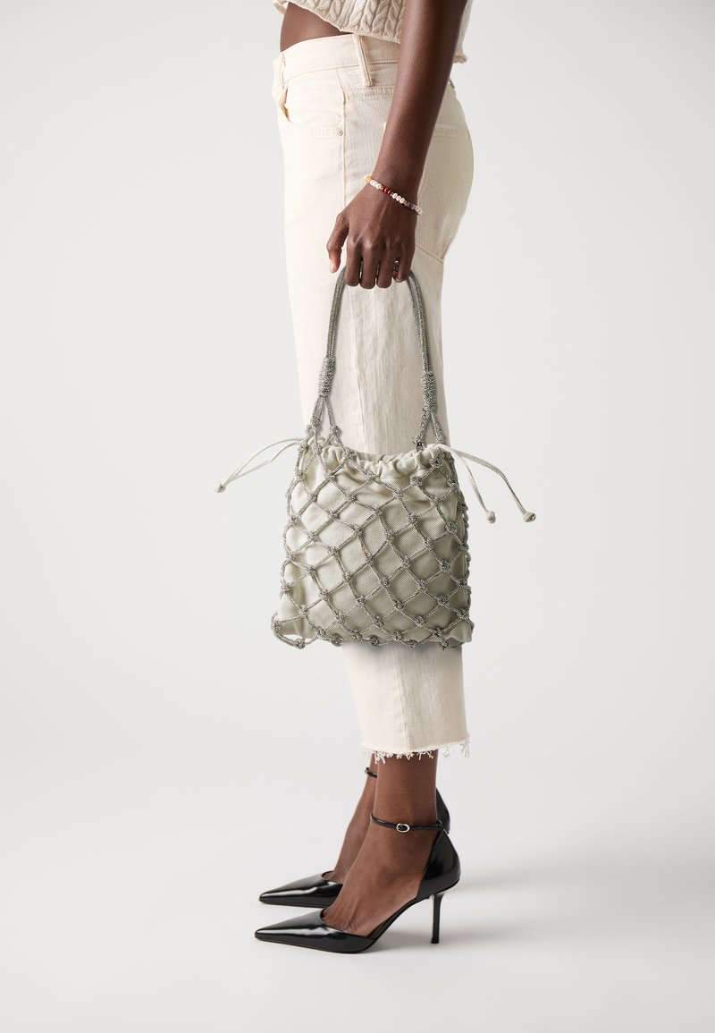 Sac en tissu vert et doux avec un motif en losanges texturé et des accents argentés, doté d'une fermeture à cordon et de poignées tressées, tenu à bout de bras.