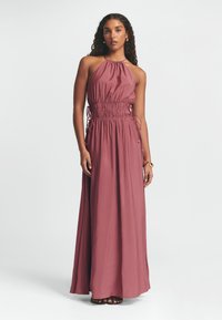 Maxi suknelė dulkėtai rožinės spalvos su kaklo lašišėle, susiaurinta liemeniu ir šoniniais raišteliais. Lygi medžiaga su laisvu siluetu.