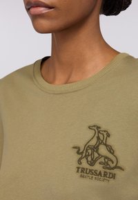 Olivegrüner Baumwoll-Sweatshirt mit einem gerippten Rundhalsausschnitt und einem gestickten Trussardi-Logo mit einem Hundemotiv auf der Brust.
