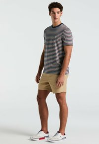 Gestreepte T-shirt met korte mouwen in blauw, rood en wit met een marineblauwe ronde hals. Gecombineerd met beige shorts en witte sneakers met rode accenten.
