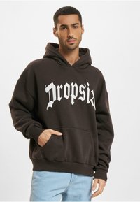 Mørkebrunt hoodie med frontlomme, der har store hvide bogstaver, som siger "Dropsia." Blødt stof, afslappet pasform og snøre i hætten.