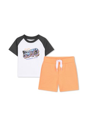 Camiseta raglán blanca y gris oscuro de manga corta con el texto "1973 Timberland" combinada con pantalones cortos naranjas con cordón para niños.