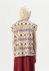Short-sleeved top in a cream base with a geometric pattern in brown, maroon, and purple stripes, featuring a rounded neckline and loose fit.