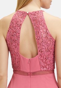 Pink dress featuring a lace back with intricate embroidery and sequins, a keyhole closure, and a fitted waist with a mesh detail.