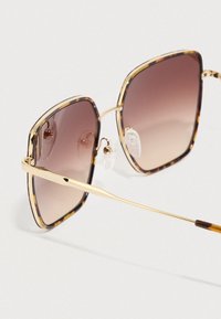 Čtvercové sluneční brýle s obroučkami vzoru želvovina a hnědými čočkami s přechodem. Zlaté kovové detaily a nastavitelná nosní opěrka pro pohodlí.