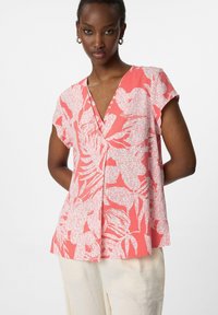 blusa corallo a maniche corte con scollo a V, caratterizzata da motivi florali bianchi e una vestibilità ampia, realizzata in un tessuto leggero.