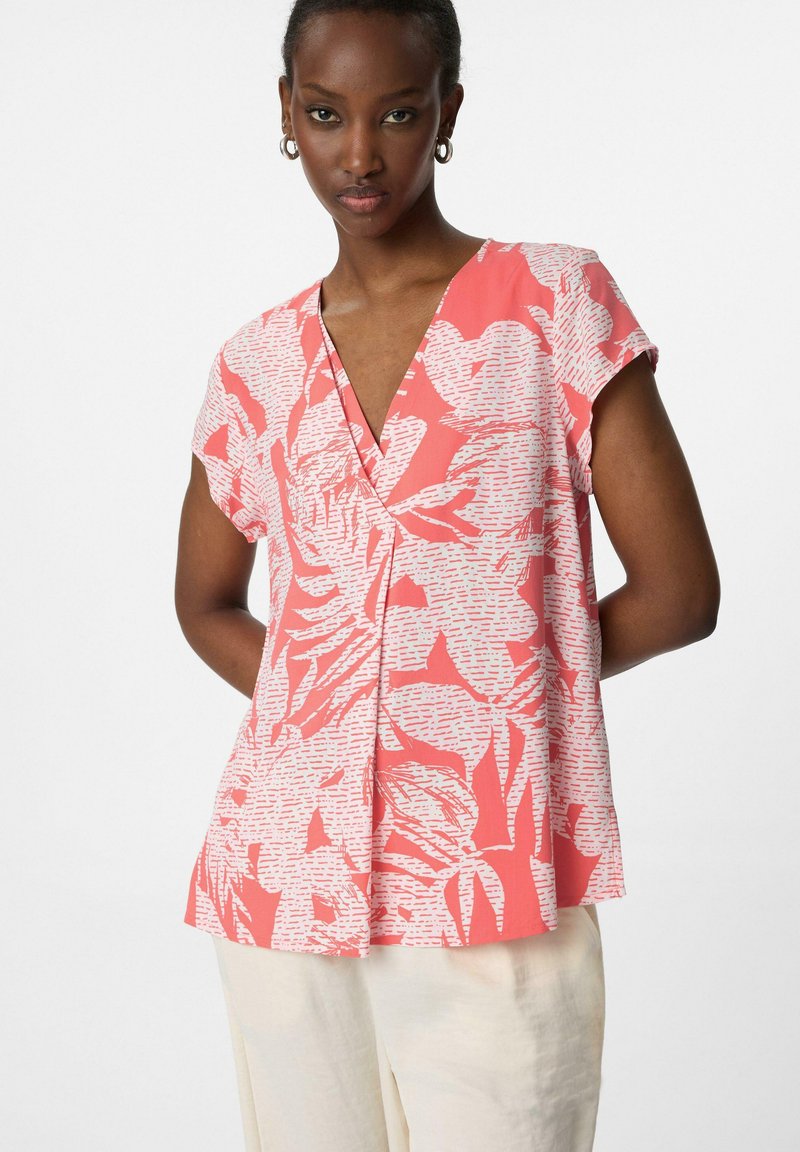 blusa corallo a maniche corte con scollo a V, caratterizzata da motivi florali bianchi e una vestibilità ampia, realizzata in un tessuto leggero.