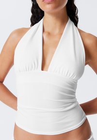 White halter neck top made of smooth fabric, featuring a plunging neckline and gathered detailing around the bust and waist for fitted shape.