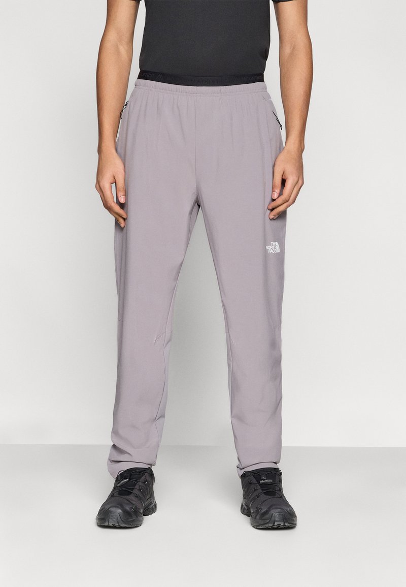 Γκρι outdoor παντελόνι με ελαστική μέση, με τσέπες στο πλάι και λογότυπο στο αριστερό μηρό. Φορεμένο με μαύρα αθλητικά παπούτσια.