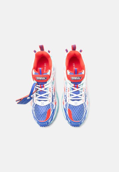 Ζευγάρι αθλητικά παπούτσια Off-White σε λευκό, μπλε και κόκκινο χρώμα με λεπτομέρειες από δίχτυ και προσαρτημένη μπλε και κόκκινη ετικέτα, σε άποψη από πάνω.
