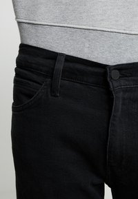 I jeans in denim nero presentano un classico design a cinque tasche, cuciture resistenti, una chiusura frontale con bottone e una texture liscia.