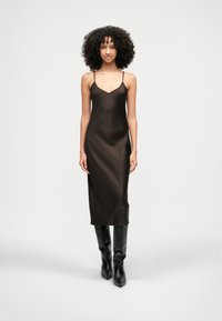 Σατέν φόρεμα σε απλή μαύρη απόχρωση, με ρυθμιζόμενες λεπτές τιράντες, V λαιμόκοψη, κομψή σιλουέτα και μήκος μίντι που φτάνει λίγο κάτω από τα γόνατα.