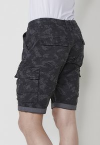 Shorts cargo noirs avec un motif texturé subtil, taille élastique et ourlet roulé. Comprend plusieurs poches latérales pour le rangement.