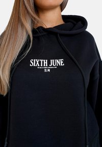 Felpa nera con cappuccio realizzata in un morbido tessuto, caratterizzata da un logo frontale "SIXTH JUNE" in testo bianco. Include un cappuccio regolabile con cordini e una vestibilità rilassata.