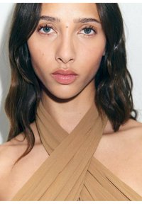 Brown, sleeveless, cross-front top made of soft fabric. The design features pleats and a neckline that highlights the shoulders.