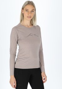 Maglietta a maniche lunghe di colore marrone chiaro, realizzata in materiale morbido, con una grafica di montagna stampata in grigio scuro sul petto. Fessure laterali per maggiore comfort.