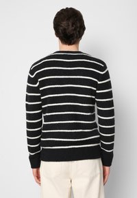 Sweter w czarno-białe paski o miękkiej teksturze, z długimi rękawami i prążkowanym wykończeniem, prezentowany z tyłu.