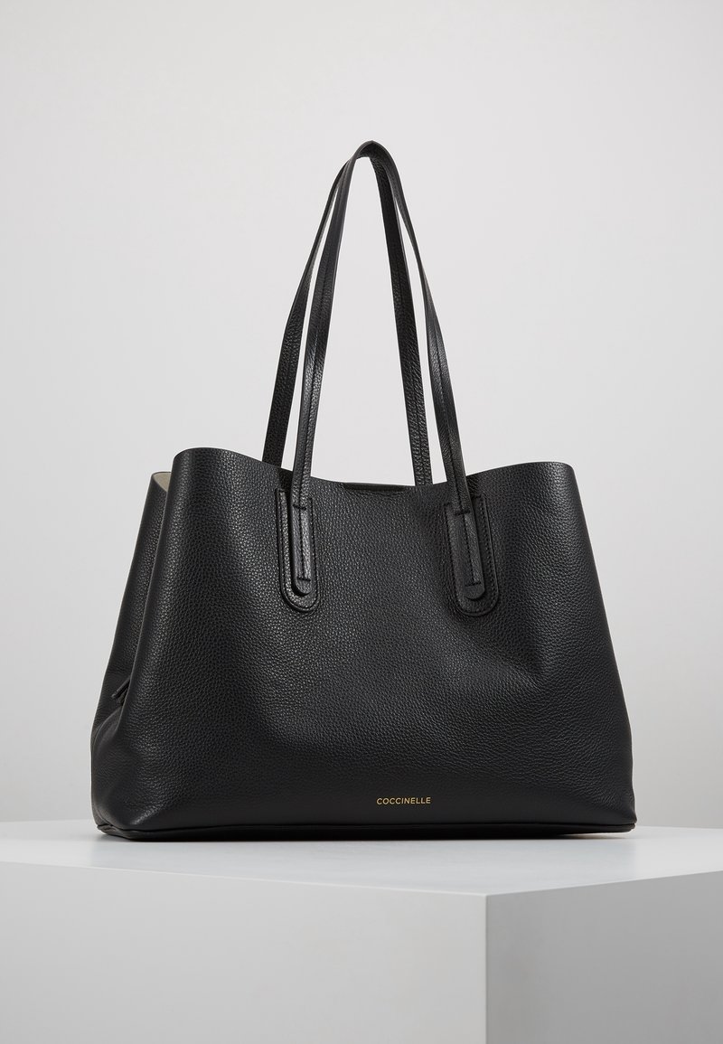 Sort læder tote taske med en tekstureret overflade, to lange håndtag, åben top og et guldlogo i bunden. Enkelt, rummeligt design.