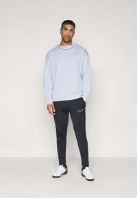 Lyseblå genser med høy hals og sølvlogo, parret med svarte tapered joggebukser med hvit Nike-logo. Hvite sneakers.