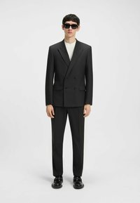 Black double-breasted suit with wide lapels, tailored fit, and matching trousers. Paired with a white t-shirt and black sunglasses.