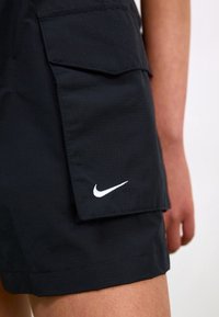 Black shorts made of lightweight fabric with a textured pattern, featuring a side pocket and a white Nike logo on the front.