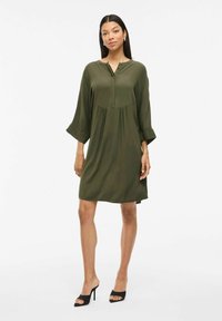 Robe verte, longueur genou, à coupe décontractée, manches longues, col boutonné et plis sous la poitrine. Tissu doux avec une texture lisse.