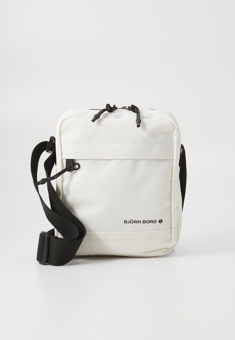 White fabric crossbody bag with a black strap, zip closure, and front pocket. Features logo printed on the lower front.