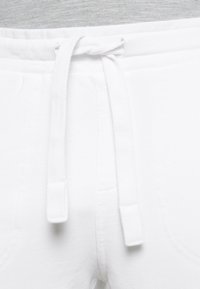 Pantalones con cinturilla elástica blanca y cordón atado, que cuentan con bolsillos laterales y una textura de algodón suave. Diseño simple y funcional.