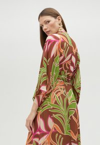 Robes longues, marron, à motifs avec des designs floraux verts, roses et oranges. Les manches fluides et la taille nouée accentuent la silhouette.