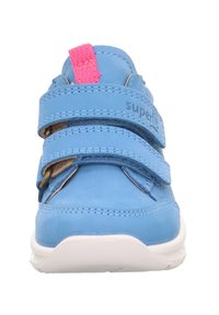 Niebieskie skórzane buty z białą podeszwą, posiadające dwa paski na rzepy i różową pętelkę z tyłu. Nazwa marki "superfit" wytłoczona na boku.