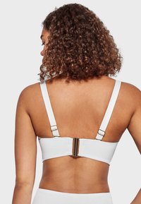 Sosten blanco con tirantes ajustables, que presenta herrajes de color dorado en la parte posterior y un diseño liso y sin costuras.
