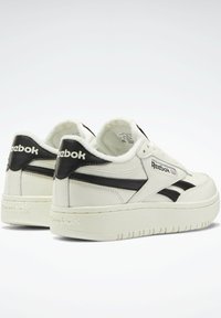 White leather sneakers with black accents, featuring a thick sole, round toe, and cushioned collar. Reebok logo on the sides and tongue.