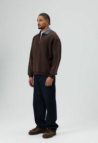 Bruine zip-up trui met een contrasterende denim kraag, gecombineerd met losse donkerblauwe spijkerbroeken en bruine wandelschoenen.