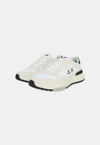 Zapatos deportivos blancos con parte superior de malla y cuero, acentos negros y suela de goma texturizada, con cordones y logo en la lengüeta.