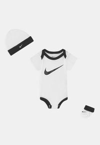 Mon body en coton blanc pour bébé avec des bords noirs et le logo Nike, accompagné d'un bonnet assorti et de chaussettes avec un bandeau noir et le logo.