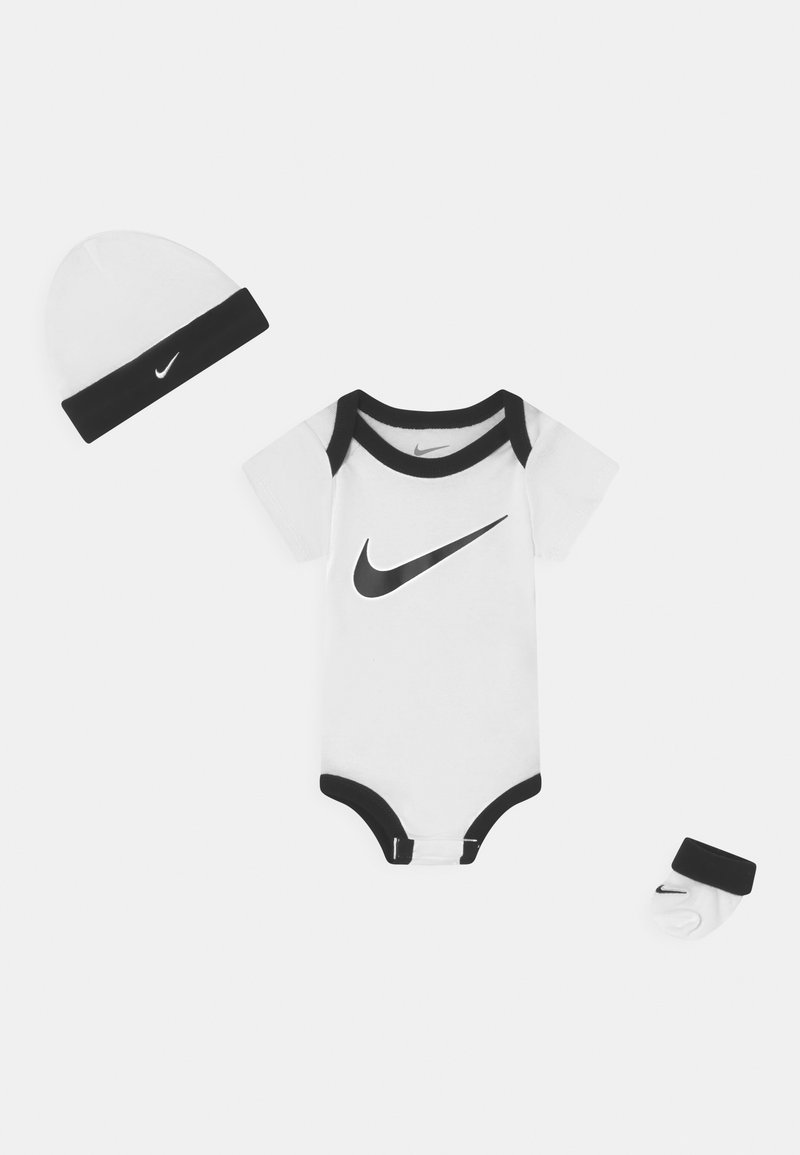 Mon body en coton blanc pour bébé avec des bords noirs et le logo Nike, accompagné d'un bonnet assorti et de chaussettes avec un bandeau noir et le logo.