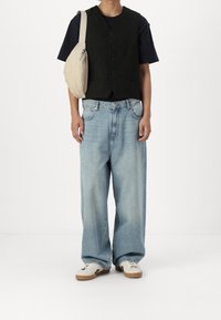 Gilet nero in lana sopra una maglietta nera, jeans azzurri a taglio largo e sneakers bianche. Indossata una borsa a tracolla beige con cerniera.