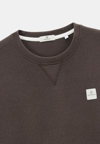 Sweat-shirt en coton marron avec un col rond, des poignets côtelés et une petite étiquette logo sur le côté gauche. Il présente un tissu texturé.