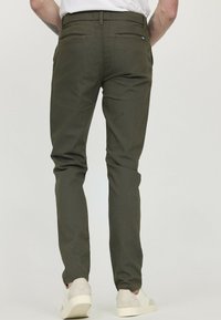 Pantalons vert olive à coupe fuselée, en tissu texturé. Dotés de poches arrière et de détails de couture subtils. Associés à des baskets légères.