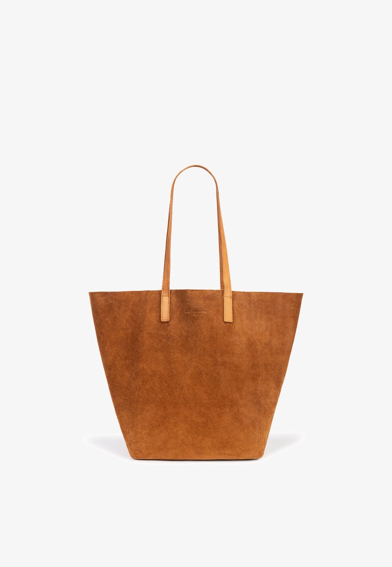 Tan suede tote bag with two long leather handles, wide base, and subtle logo detail on the front. Smooth texture, minimalist design.