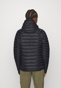 Zwarte gewatteerde jas met capuchon, voorzien van doorgestikte secties, een gladde textuur en een getailleerd ontwerp dat naar de taille toe smaller wordt.