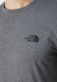 Sivi pamučni majica s okruglim izrezom, s crnim tiskanim logotipom "THE NORTH FACE" na lijevoj strani prsnog dijela. Mekana tekstura.