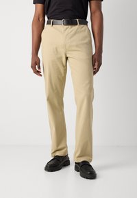 Beige katoenen chino's met een rechte snit, ritssluiting en zijzakken, gecombineerd met een zwarte leren riem en zwarte schoenen.
